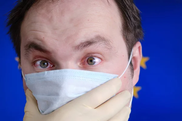 A man in a medical mask with red eyes on the background of the European flag