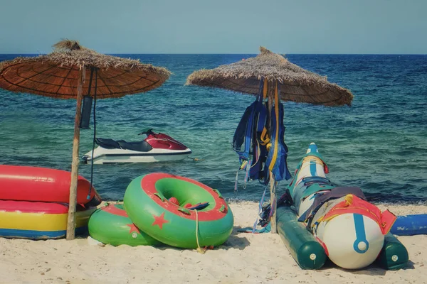 Inflatable circle, mattress and banana under umbrella on sand beach. Bad weather and water rides do not work