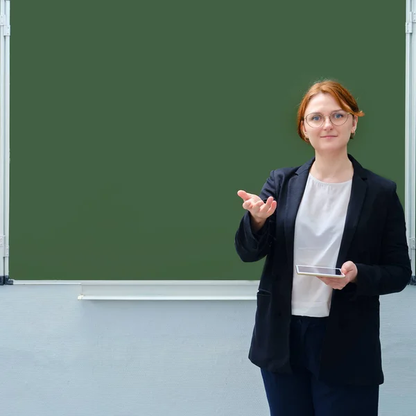 An empty blackboard with a copy space for text and the teacher shows a hand gesture of welcome. Back to school concept