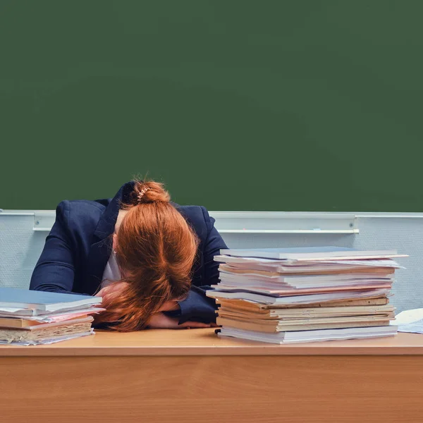 Female teacher crying with her head bowed on the desk, copy space. Sad school teacher on the background of a green blackboard, close-up