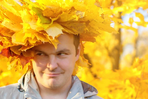 Portrait of a young man with a wreath of yellow leaves on his head. Autumn portrait of a man against the yellow leaves of a tree.