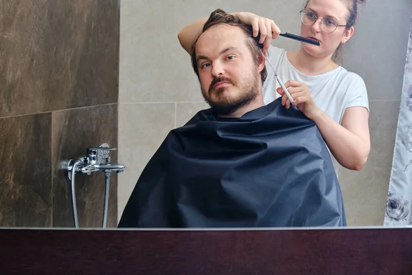 A woman cuts a man\'s hair at home in the bathroom, reflection in the mirror, copy space