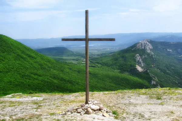 Catholic wooden cross on the background of green mountains. Christian Church symbol on the top of the hill. Religious sign on top of the mountain. A simple wooden cross on a Sunny day.