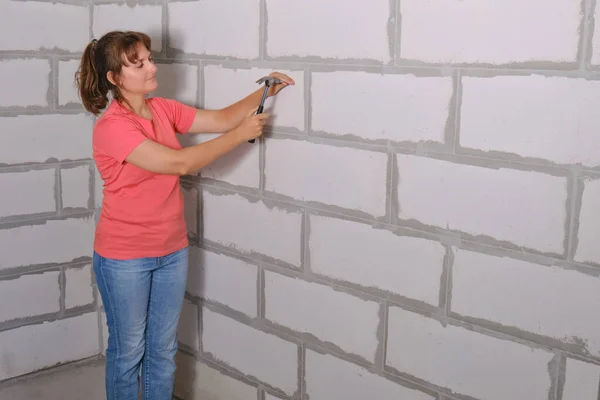 A young woman with a hammer hammering a nail into the wall of foam blocks. Repair with your own hands in a new apartment, copy space. The creation of the interior himself built in the house.