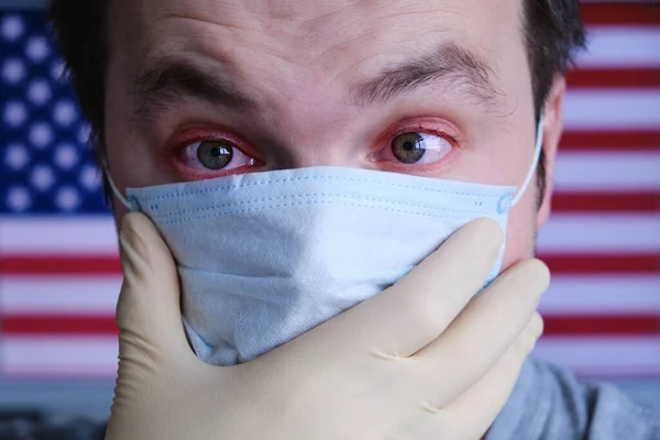 Portrait of a man in a medical mask on the background of the USA flag, copy space for text