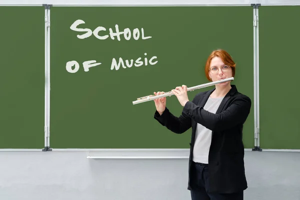 A music teacher plays the flute. Learning to play wind musical instruments against a blackboard with the text Music School