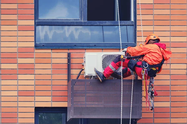 A man in a red uniform connects the air conditioner under the apartment window