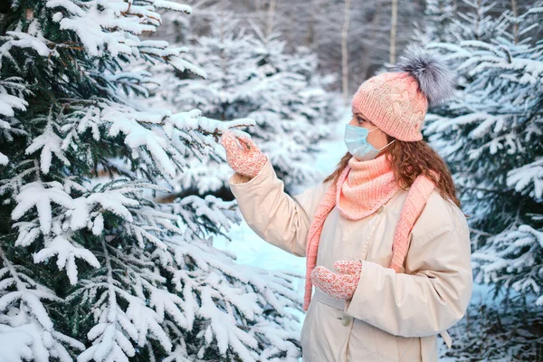 A woman in face mask chooses a live Christmas tree in the forest for the new year. Concept of coronavirus problems for the new year.