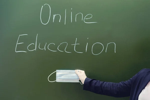 Teacher hand with medical mask and text Online education on the school blackboard. Problems of online training in quarantine during the coronavirus pandemic