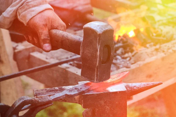 Blacksmith hammer hits the hot metal. Forging of iron objects in a retro forge. The process of working on the manufacture of weapons blacksmith on the anvil.