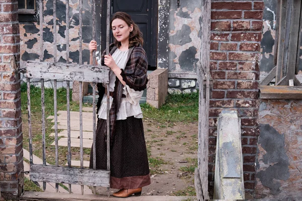 A young woman in vintage clothes sings a song near the old gate. Retro dress on Halloween style 18-19th century