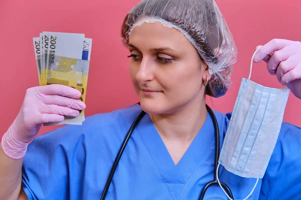 A woman medical doctor holds cash euros in her hands. A nurse with money in a protective mask on a pink background.