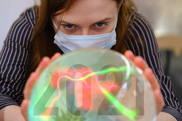 A gypsy woman wonders about the future of the coronavirus in 2021 on the ball of fate. Witch in a face mask over a crystal ball predicts the future of the flu virus in the new year