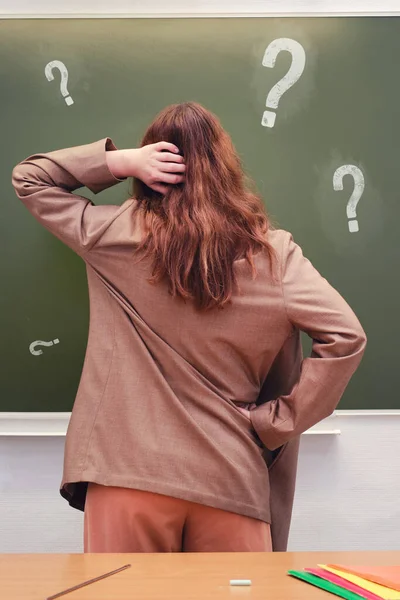 Woman teacher indecisively stands at the blackboard, copy space