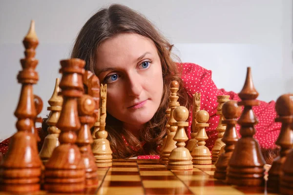 Adult woman playing chess while sitting on the bed at the chessboard, face close up