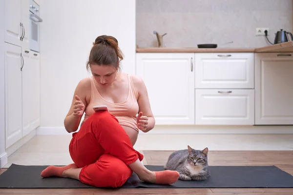 Sports activities during pregnancy and problems lessons online. A woman with a phone is studying fitness over the Internet in a home kitchen