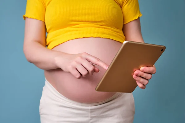 Digital tablet in the hands of a pregnant woman on a blue background