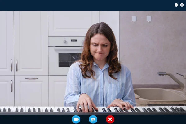 Angry woman plays the piano while sitting in a home kitchen in an online video chat. Screen with chat and video call interface