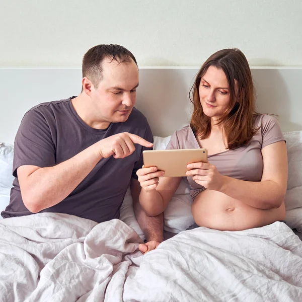 A smiling man and a pregnant woman watch training on a tablet over the Internet