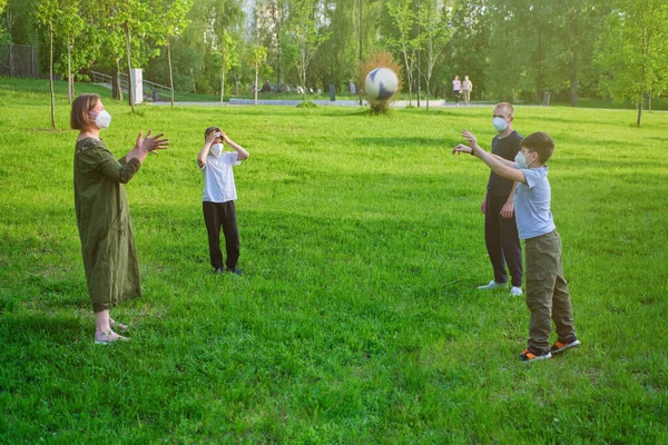 Family in face medical masks play sports with a soccer ball in nature