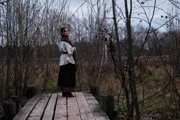 Full-length woman on an old wooden platform from boards in retro style. Vintage clothes on the woman, dress and linen white shirt.