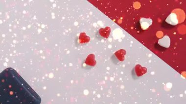 Küçük beyaz konfeti parçalarından oluşan romantik bir patlama koyu arkaplanda parıldayan kırmızı kalplerin üzerine patlayıcı bir şekilde yağar. Sevgililer Günü için mükemmel, aşk, romantizm, kutlama, evlenme teklifi ve düğün teması.