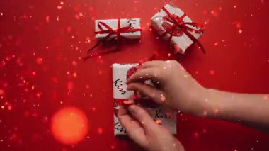 Sevgililer Günü hediye kutusunda kurdele bağlayan ellerin yakın plan videosu kırmızı arkaplanda canlı renkli konfeti parçalarıyla son buluyor. Romantizm, kutlama ve festival promosyon projeleri için mükemmel..