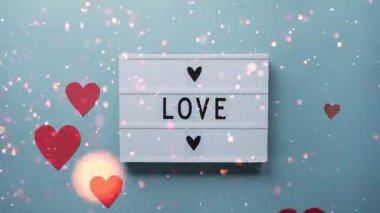 Romantik bir Sevgililer Günü videosu. Sevgi sözcüğüne sahip canlı kırmızı bir kalp koyu mavi bir arka planda oturur. Renkli bir konfeti ve sim parçacıkları kutlayıcı ve neşeli bir animasyonda kalbin üzerinde patlar..