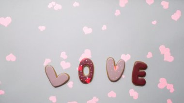 Kalp şeklinde kurabiyeler ve pembe arka planda serpiştirilmiş şekerler. Sevgililer Günü konsepti