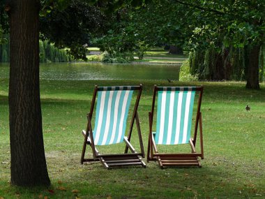 Londra 'daki St. James' s Park 'taki bir ağacın altında göle bakan iki çizgili iskemle. Yüksek kalite fotoğraf