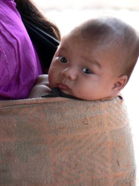 Annesinin sırtındaki sevimli Lao bebeğini kameraya bakarken yaklaş. Yüksek kalite fotoğraf