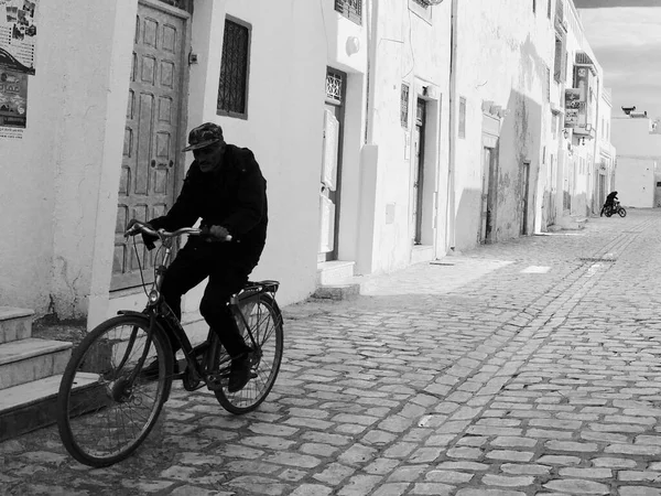 Black and white shot of man on bike ridding through cobbled street. High quality photo