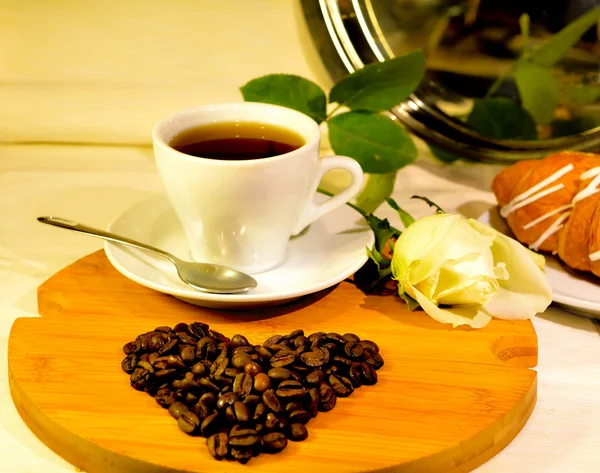 Taza de café con el corazón de los granos de café y rosa blanca — Foto de Stock