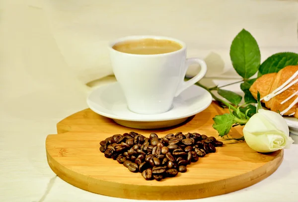 Naturaleza muerta: declaración de amor. Taza de café de la mañana con el corazón de los granos de café y rosa blanca — Foto de Stock