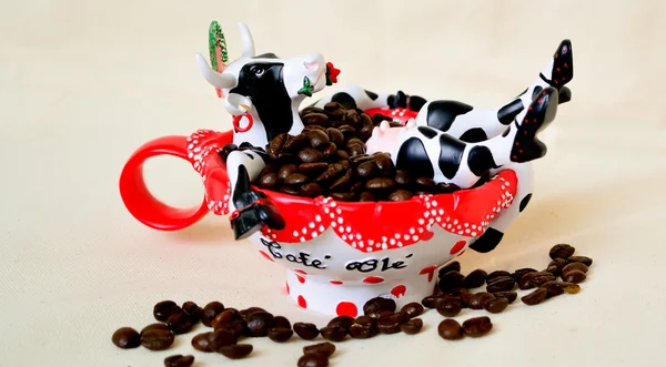 Café blanco - Juguete de vaca de cerámica en la corona sentado en la taza roja con granos de café como en el baño — Foto de Stock