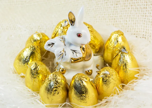 Huevos de Pascua de chocolate en cubierta dorada brillante y conejo de porcelana — Foto de Stock