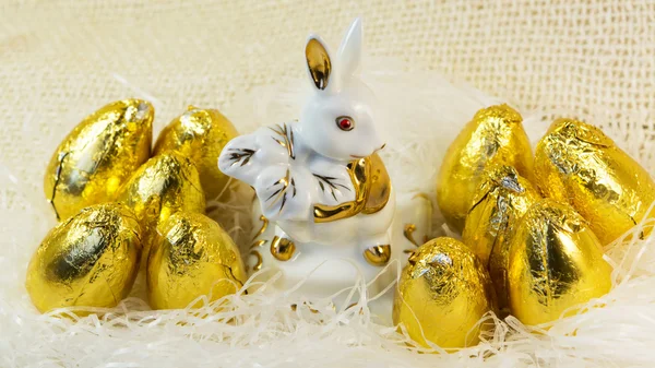 Huevos de Pascua de chocolate en cubierta dorada brillante y conejo de porcelana — Foto de Stock