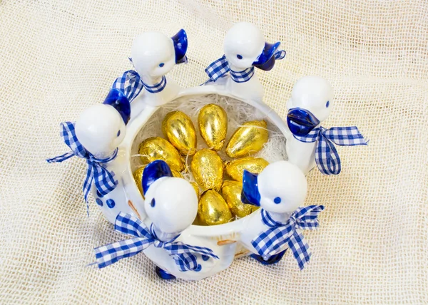 Ovos de Páscoa de chocolate em tampa dourada brilhante em branco com vaso azul com figuras de patos — Fotografia de Stock