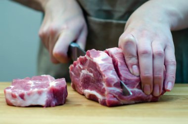 Mutfaktaki hostes bıçakla domuz pirzolası doğruyor. Kesme tahtasında et, biftek hazırlığı, tatil hazırlığı. Baharat, acı biber, biberiye. Gıda arkaplanı