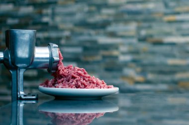 Metal elle öğütülmüş et öğütücüsünde öğütülmüş kırmızı et. Fotokopi alanı olan tuğla bir duvarın arka planında yakın plan.