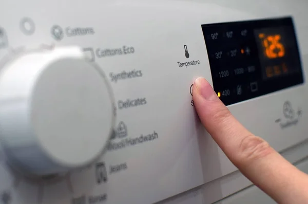 Photo d'une femme installant la machine à laver, ajustant les paramètres de lavage, allumant le lavage. — Photo