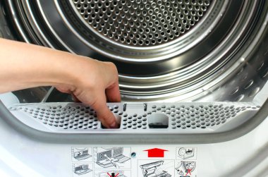 Bir ev hanımı, ön yükleme makinesinden iplik tuzağı tutar. Bir kadının eli kurutucudan filtreyi çıkardı.