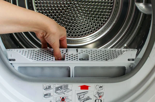 Bir ev hanımı, ön yükleme makinesinden iplik tuzağı tutar. Bir kadının eli kurutucudan filtreyi çıkardı.