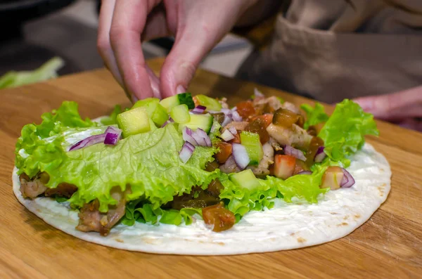 Delicious lavash rolls with fried chicken and vegetables on a wooden cutting board. Cooking process, close-up. — Fotografia de Stock