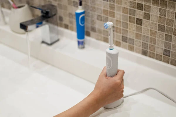 Рука с электрической зубной щеткой на заднем плане ванной комнаты — стоковое фото