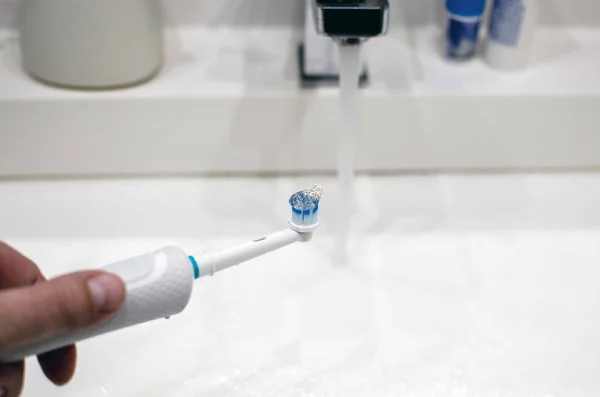 Hand with an electric toothbrush on a light background, charger — Stock Photo, Image