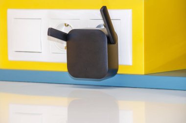 WiFi repeater in an electrical outlet on a yellow wall. An easy way to extend your wireless network at home clipart