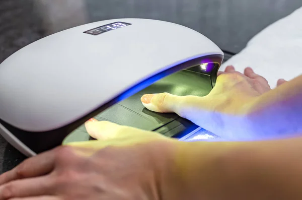 Woman hand inside nail lamp on table close-up. UV lamp for drying nails using the gel method. purple nails dried in a lamp