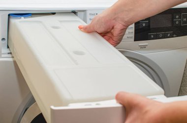 Kurutucudan çıkan bir konteynır, bir kadın kurutucudaki giysileri kuruttuktan sonra birikmiş su dolu bir tankı çıkarır..