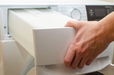 Kurutucudan çıkan bir konteynır, bir kadın kurutucudaki giysileri kuruttuktan sonra birikmiş su dolu bir tankı çıkarır..